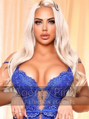A photo of escort Amira standing by the bed in her blue bodysuit Picture 1